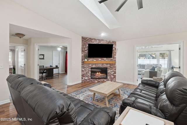 living room featuring hardwood / wood-style floors, a brick fireplace, ceiling fan, lofted ceiling, and a textured ceiling