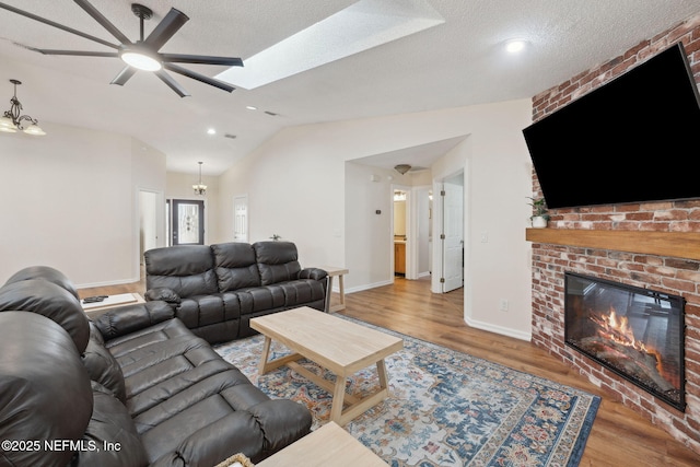 living room with ceiling fan with notable chandelier, a textured ceiling, wood-type flooring, a fireplace, and vaulted ceiling