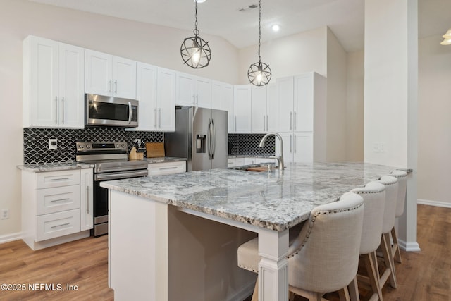 kitchen with stainless steel appliances, pendant lighting, a kitchen bar, and white cabinetry