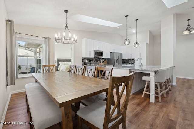 dining space featuring an inviting chandelier, vaulted ceiling with skylight, dark hardwood / wood-style flooring, and sink