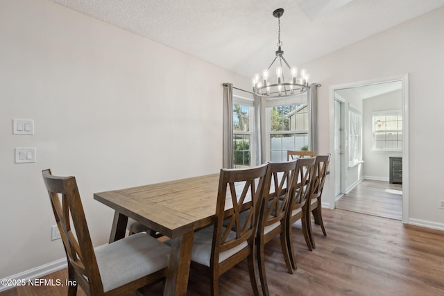 dining space with vaulted ceiling, a chandelier, a textured ceiling, and wood-type flooring