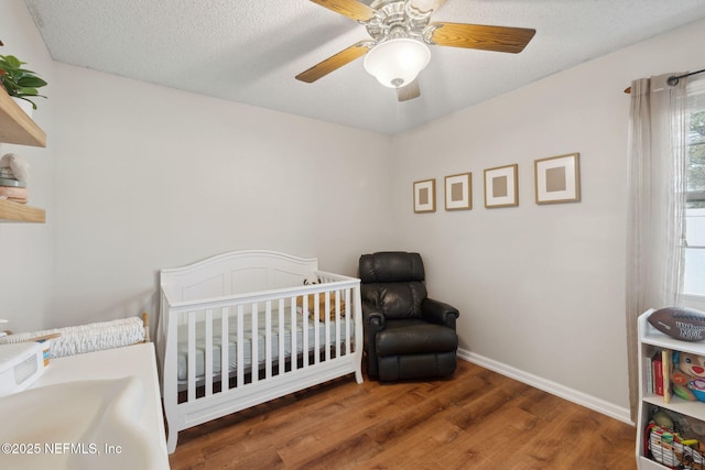 bedroom with dark wood-type flooring, ceiling fan, a textured ceiling, and a nursery area