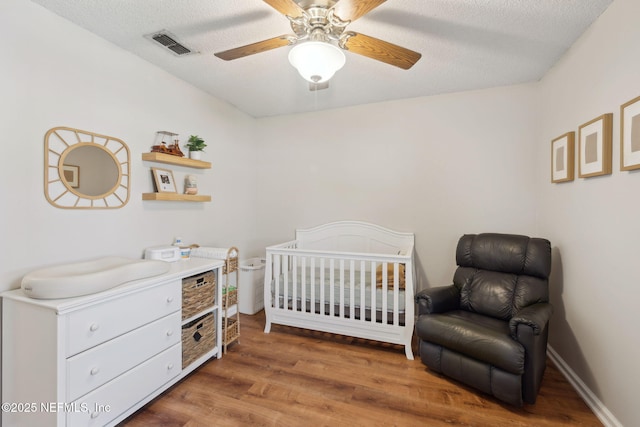 bedroom featuring ceiling fan, a textured ceiling, dark hardwood / wood-style flooring, and a crib