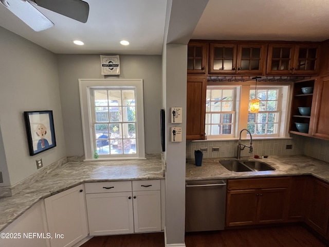 kitchen featuring backsplash, stainless steel dishwasher, glass insert cabinets, a sink, and light stone countertops