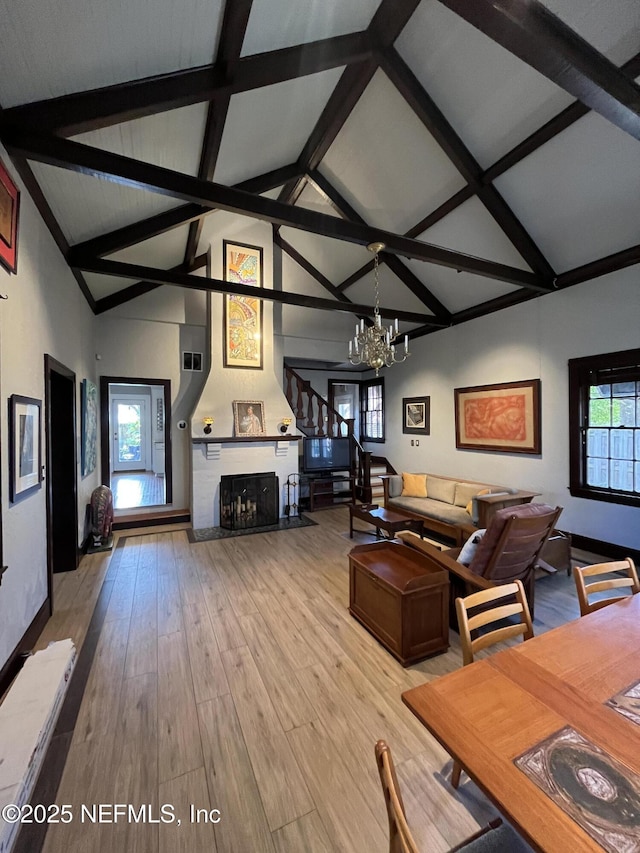 unfurnished living room with beam ceiling, a notable chandelier, a large fireplace, wood finished floors, and high vaulted ceiling