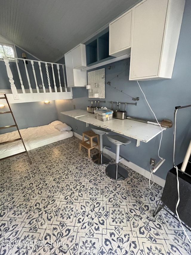 kitchen featuring light countertops, lofted ceiling, white cabinetry, and baseboards