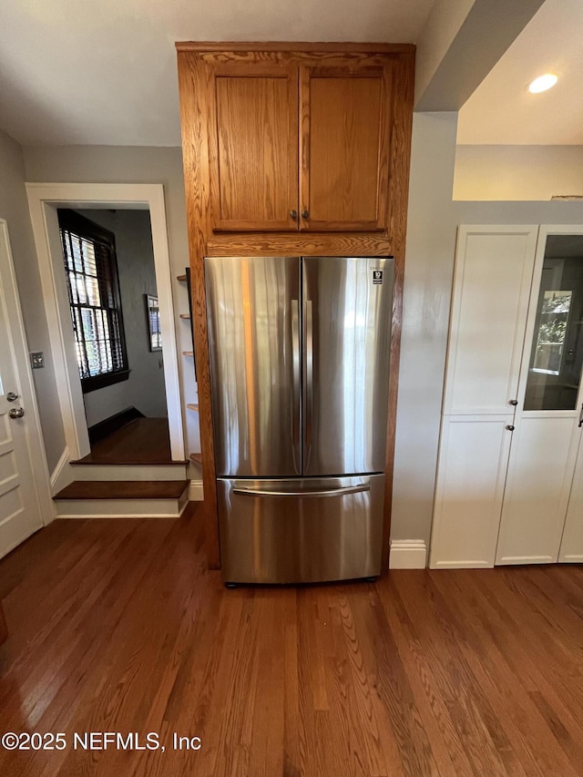 kitchen featuring brown cabinetry, freestanding refrigerator, dark wood-style flooring, and baseboards