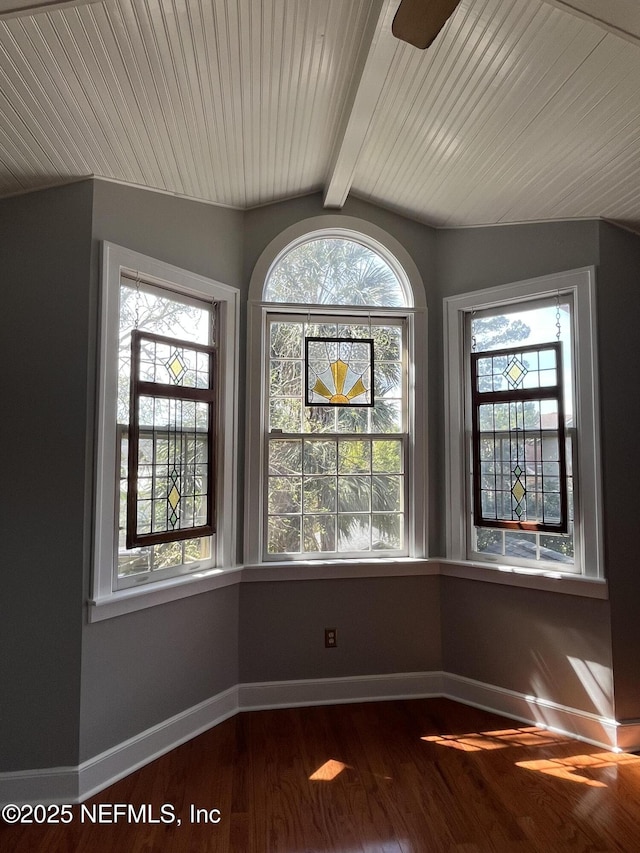 spare room featuring dark wood-style floors, a wealth of natural light, vaulted ceiling with beams, and baseboards