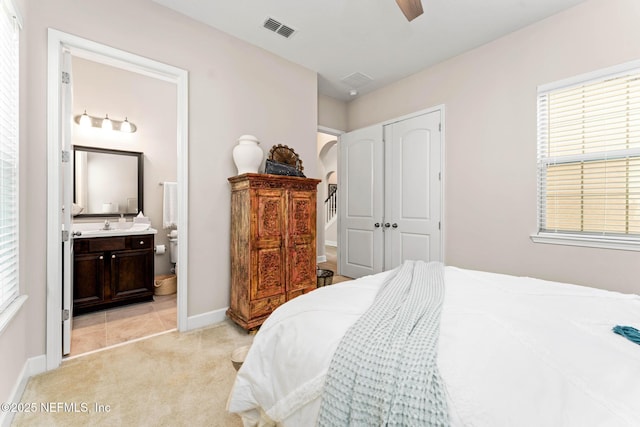 bedroom with sink, light colored carpet, ceiling fan, ensuite bath, and a closet