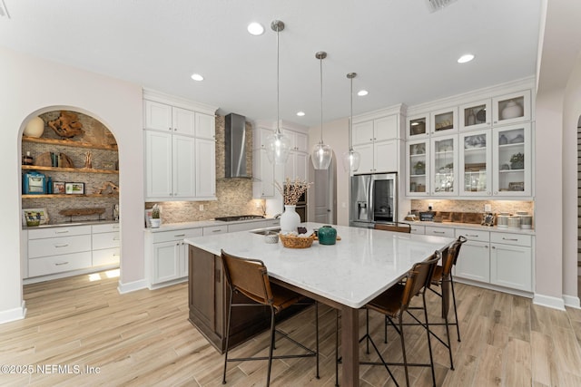 kitchen with appliances with stainless steel finishes, pendant lighting, white cabinets, a center island, and wall chimney exhaust hood