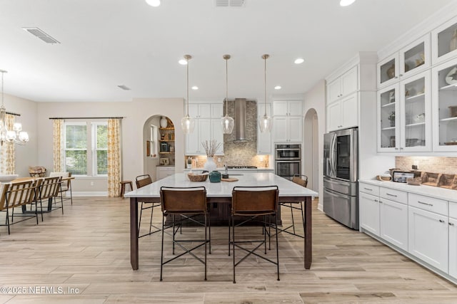 kitchen featuring stainless steel appliances, hanging light fixtures, wall chimney exhaust hood, and a spacious island