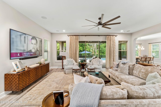 living room with ceiling fan with notable chandelier and light hardwood / wood-style flooring