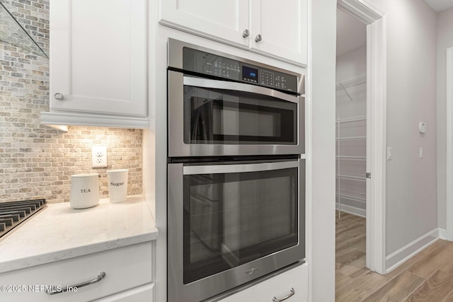 kitchen featuring light stone counters, double oven, backsplash, and white cabinets