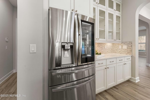 kitchen featuring stainless steel fridge, tasteful backsplash, light stone countertops, light hardwood / wood-style floors, and white cabinets