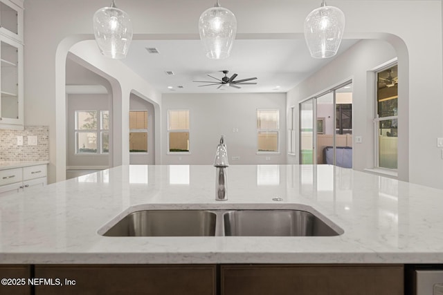 kitchen featuring light stone counters, decorative light fixtures, sink, and a center island with sink