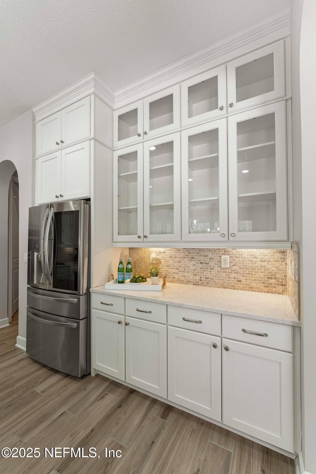 kitchen with white cabinetry, light hardwood / wood-style flooring, stainless steel refrigerator, and tasteful backsplash