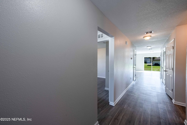 hall featuring baseboards, dark wood-style floors, visible vents, and a textured ceiling