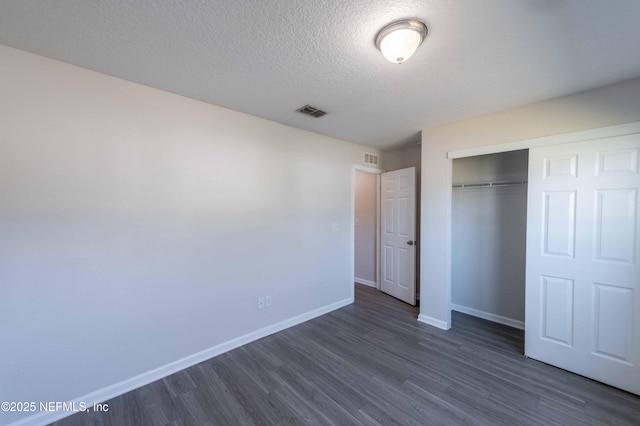 unfurnished bedroom featuring dark wood-style floors, visible vents, a closet, and baseboards