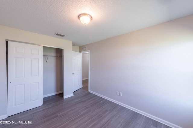 unfurnished bedroom with visible vents, a textured ceiling, dark wood finished floors, a closet, and baseboards