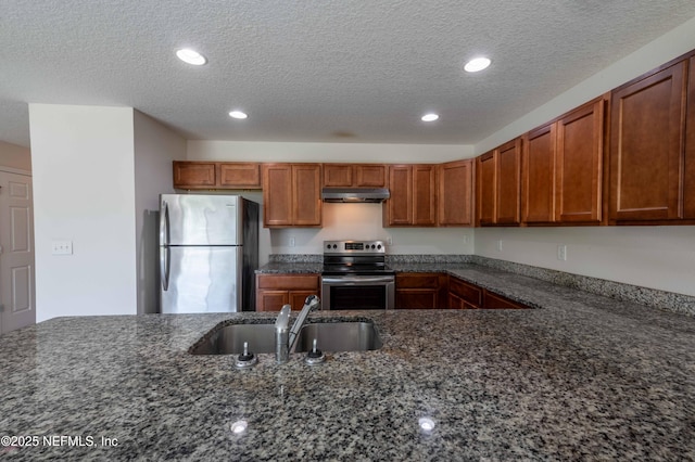 kitchen featuring dark stone counters, a sink, stainless steel appliances, under cabinet range hood, and brown cabinets