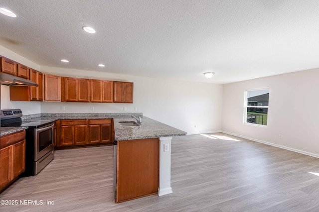 kitchen featuring under cabinet range hood, brown cabinets, stainless steel range with electric cooktop, stone countertops, and a sink