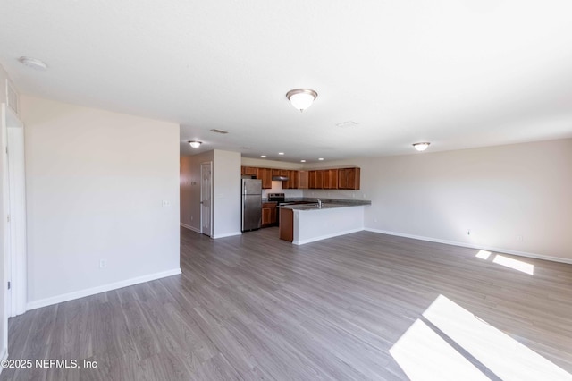 kitchen with baseboards, open floor plan, brown cabinets, freestanding refrigerator, and wood finished floors