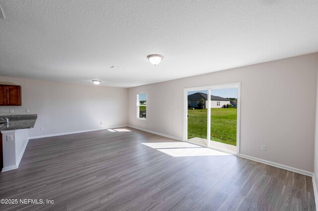 unfurnished living room with dark wood-style floors, a textured ceiling, and baseboards