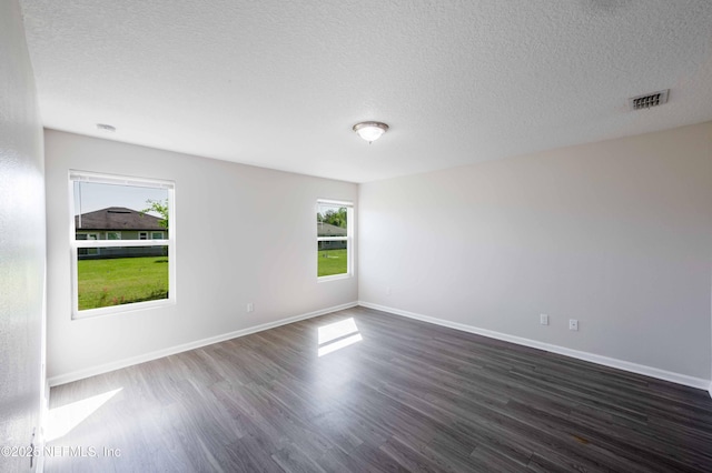 empty room featuring dark wood-style floors, visible vents, a textured ceiling, and baseboards