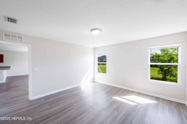 unfurnished room featuring visible vents, plenty of natural light, and dark wood-type flooring