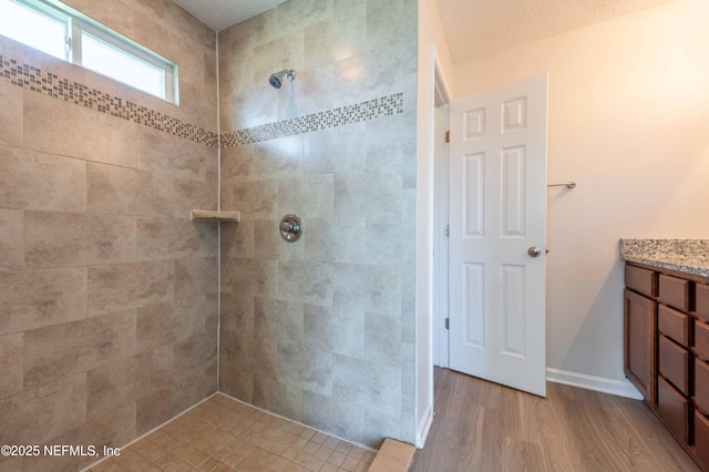 bathroom with vanity, wood finished floors, baseboards, and a tile shower