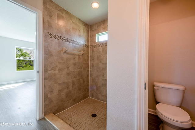 full bath with a wealth of natural light, toilet, tiled shower, and baseboards