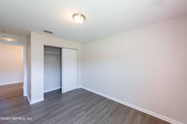 unfurnished bedroom with a closet, visible vents, dark wood-type flooring, and baseboards