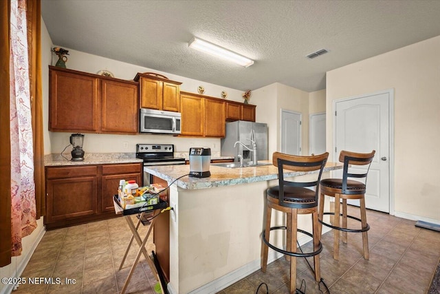 kitchen with a textured ceiling, stainless steel appliances, sink, a center island with sink, and a breakfast bar area