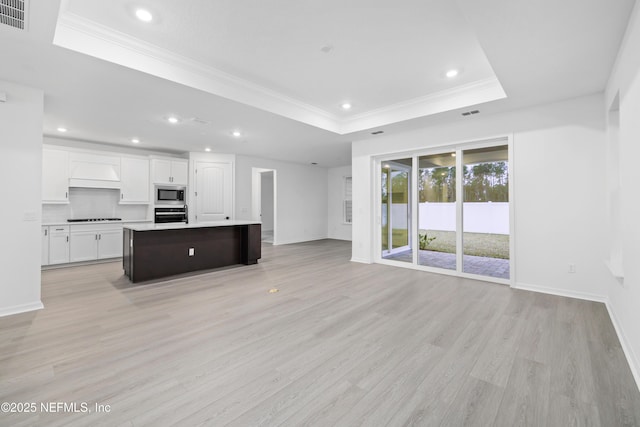 kitchen featuring light wood-type flooring, a raised ceiling, an island with sink, stainless steel appliances, and white cabinets