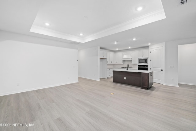 kitchen featuring a center island with sink, stainless steel microwave, a tray ceiling, black oven, and white cabinets