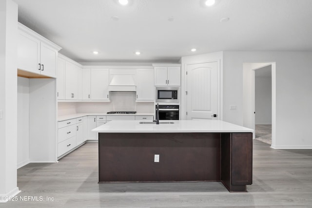 kitchen with white cabinets, a kitchen island with sink, stainless steel microwave, and oven