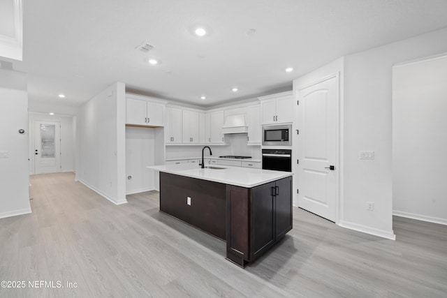 kitchen featuring stainless steel microwave, light hardwood / wood-style floors, white cabinets, a center island with sink, and oven