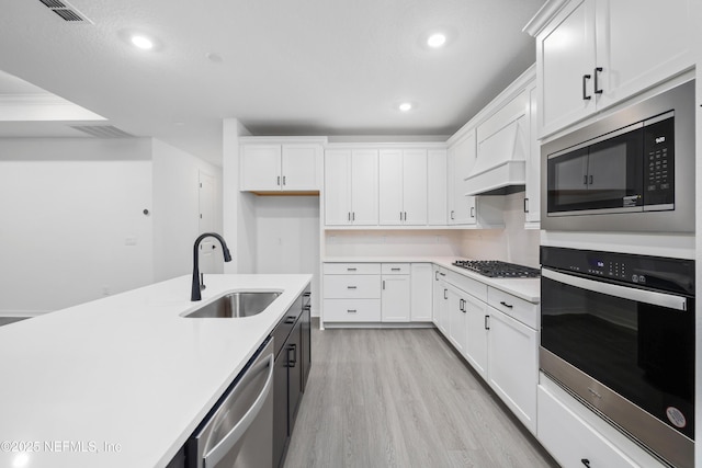 kitchen with sink, light hardwood / wood-style flooring, stainless steel appliances, white cabinets, and custom exhaust hood