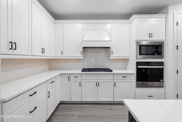 kitchen featuring white cabinetry, appliances with stainless steel finishes, custom range hood, and light wood-type flooring