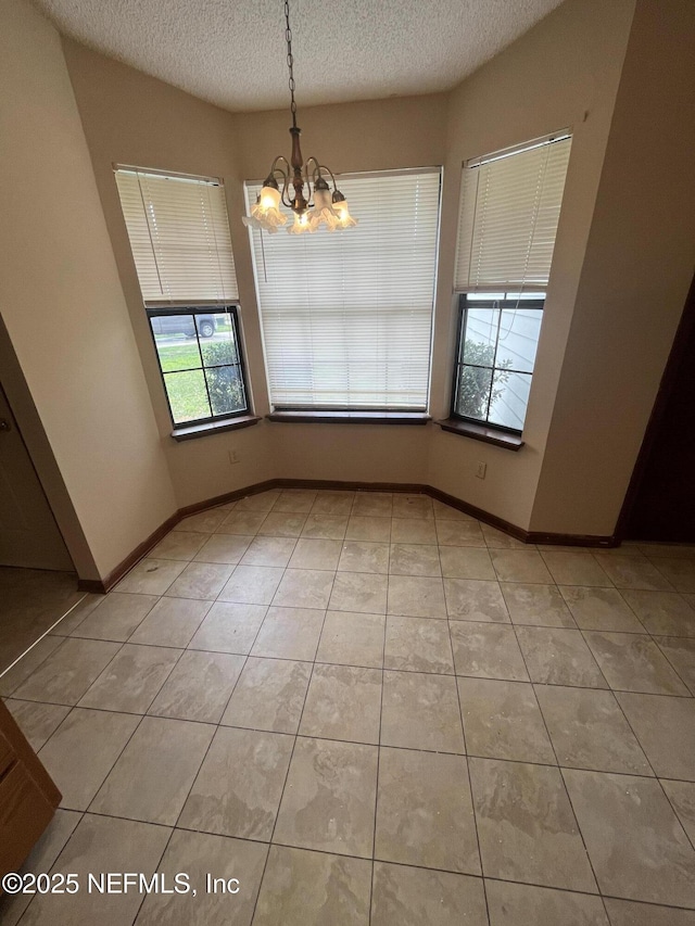 empty room with light tile patterned floors, baseboards, a textured ceiling, and an inviting chandelier