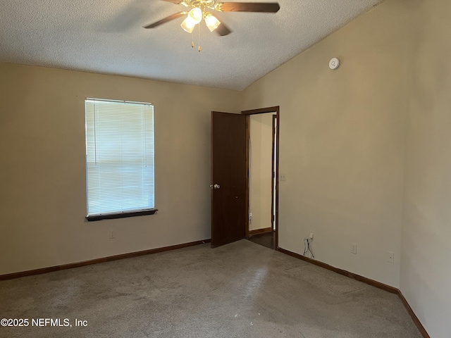 carpeted empty room with ceiling fan, vaulted ceiling, baseboards, and a textured ceiling