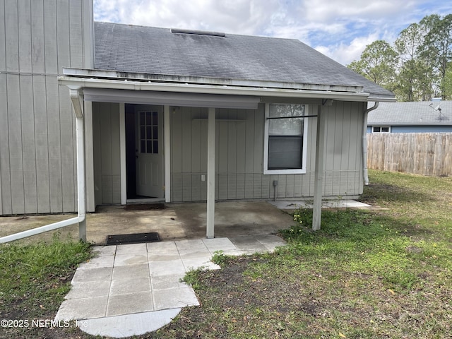 doorway to property with a patio area, roof with shingles, and fence