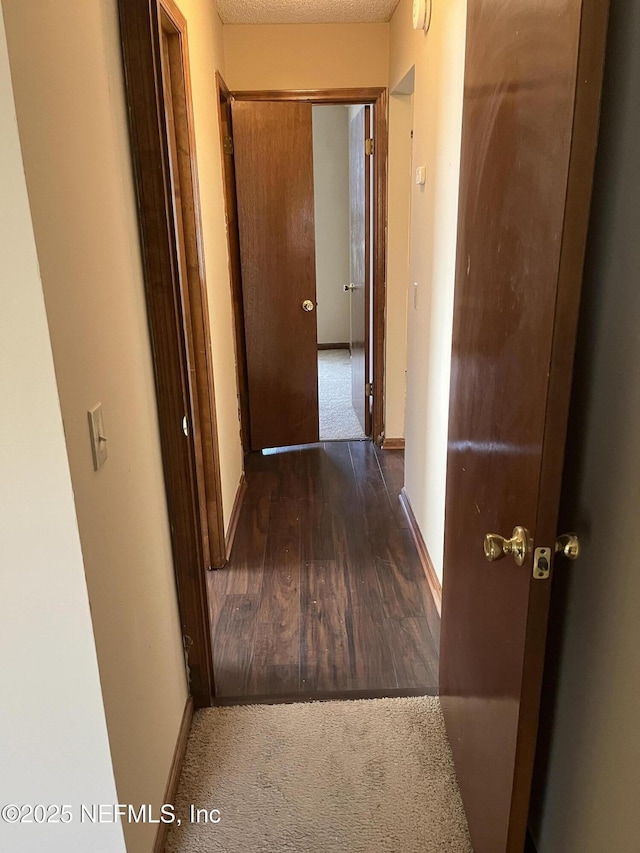 corridor featuring baseboards, carpet floors, and wood finished floors