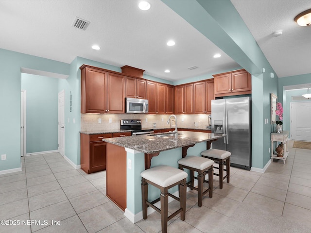 kitchen with appliances with stainless steel finishes, sink, a breakfast bar area, dark stone counters, and a center island with sink