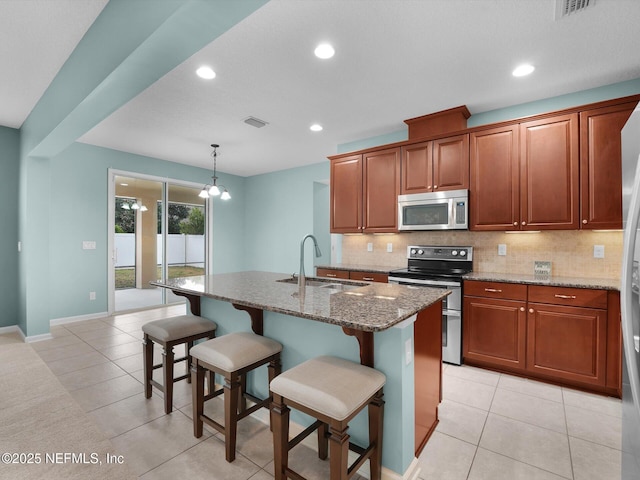 kitchen featuring sink, an island with sink, pendant lighting, stainless steel appliances, and light stone countertops