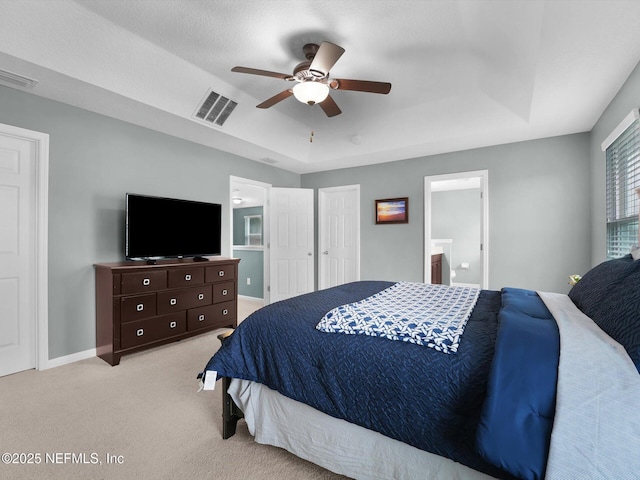 bedroom with light carpet, connected bathroom, a tray ceiling, and ceiling fan