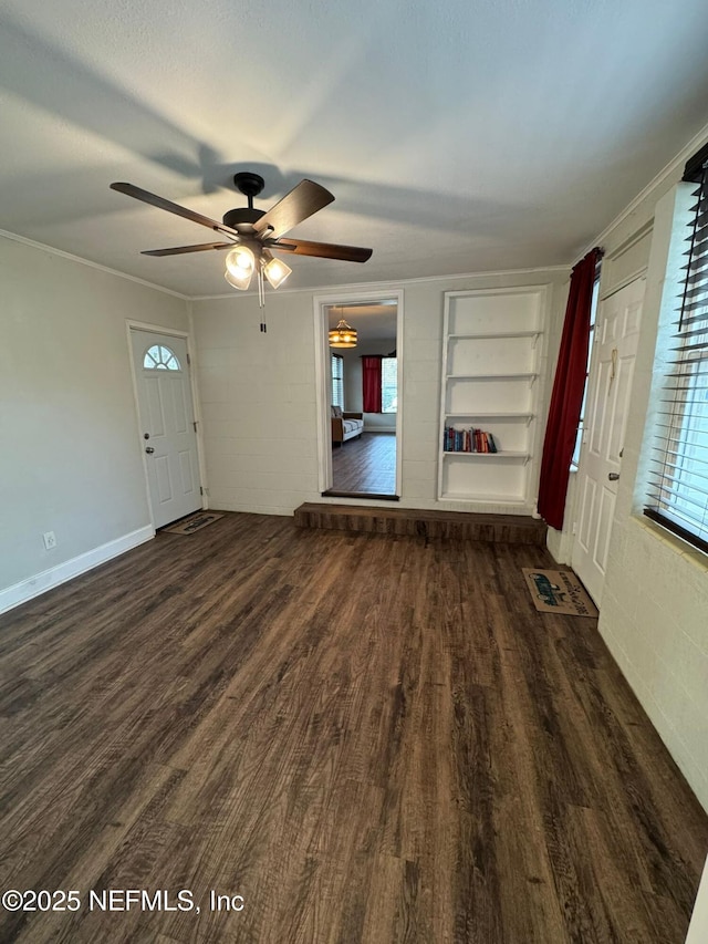 unfurnished living room featuring ceiling fan, built in shelves, dark hardwood / wood-style floors, and ornamental molding