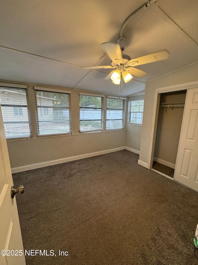 unfurnished bedroom with ceiling fan, a closet, lofted ceiling, and dark colored carpet