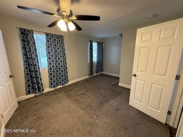 empty room featuring ceiling fan, dark carpet, and a textured ceiling