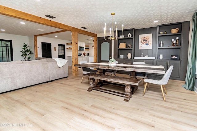 dining space featuring built in shelves, light hardwood / wood-style flooring, a textured ceiling, and beamed ceiling